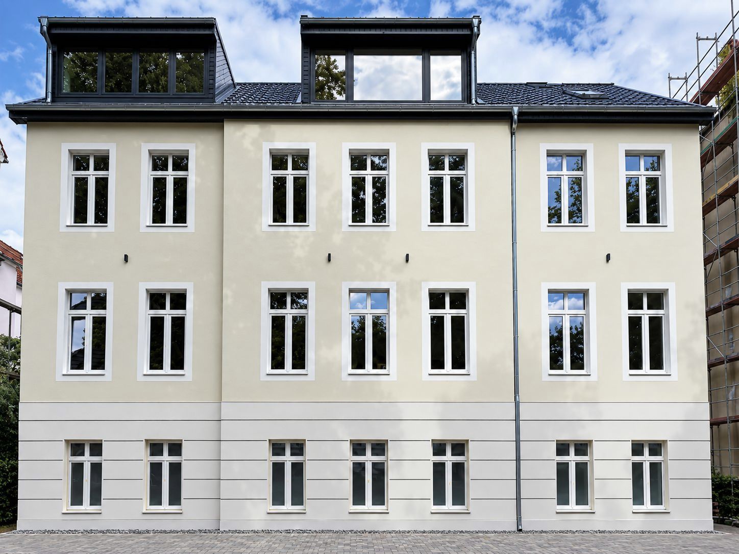 Sanierter Altbau mit heller Putzfassade, weißen Sprossenfenstern und dunklem Dach mit zwei Gauben